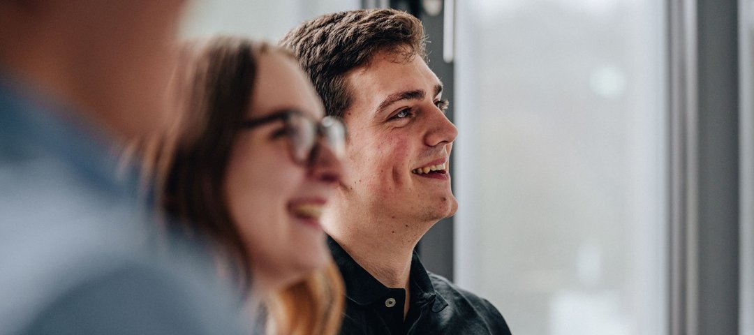Two young dual students smile as they take part in a conversation in a light-flooded room.