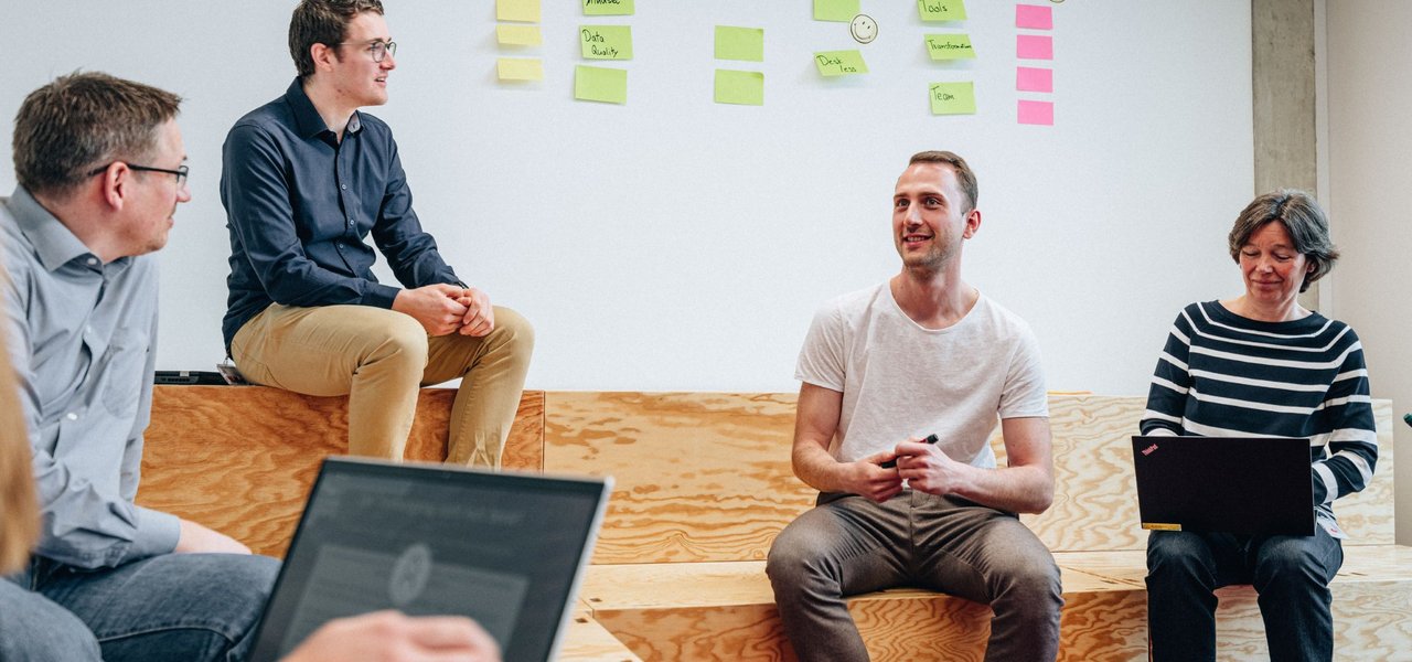 Employees have a discussion in a modernly designed workspace in front of a structured post-it wall. The picture represents creative work processes and agile methods in the everyday work at Daimler Truck.